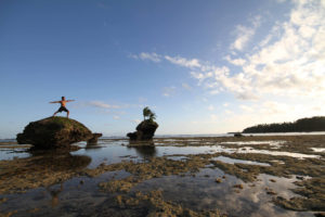 person doing warrior yoga pose on top of a rock