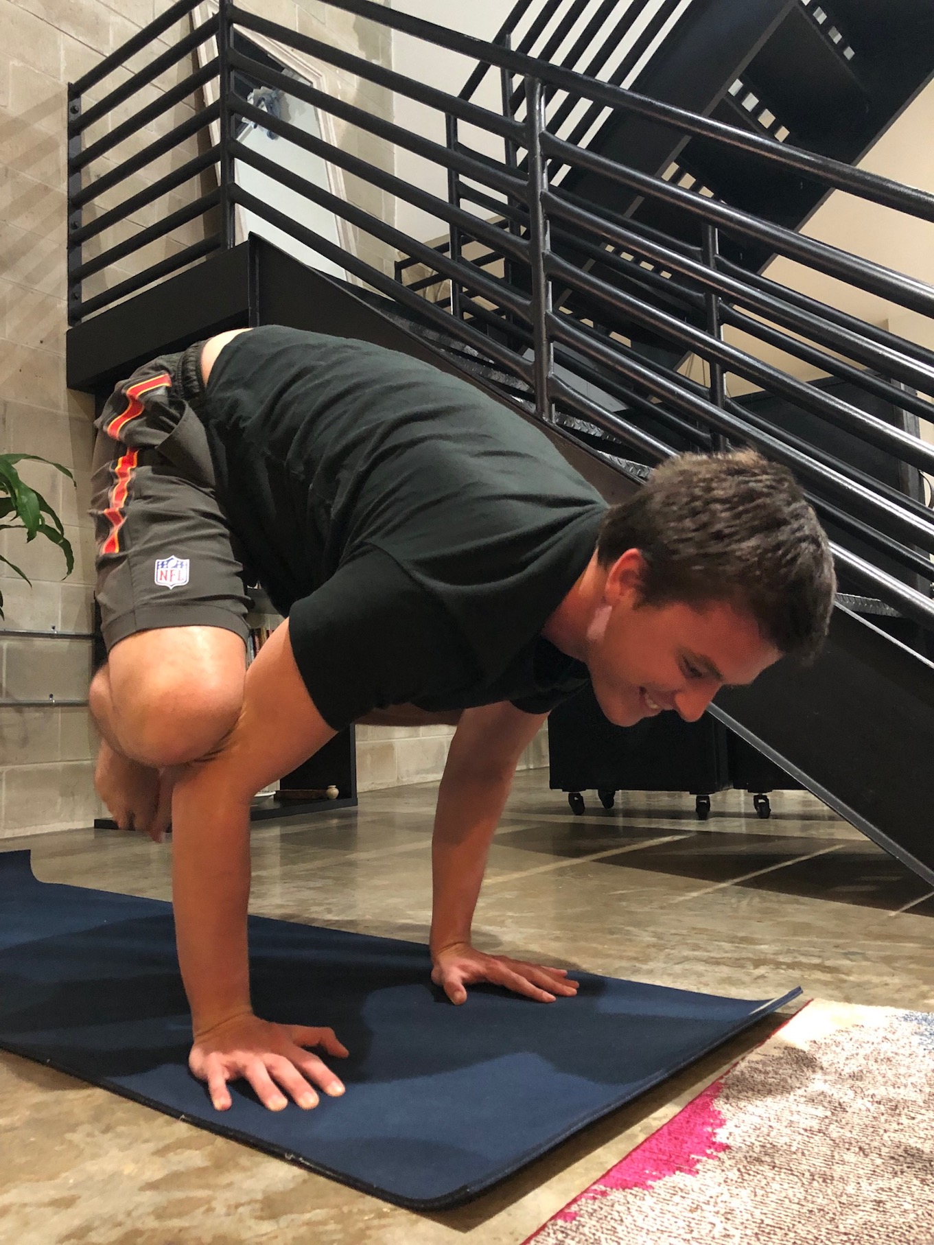 man doing crane yoga pose with stairs behind him