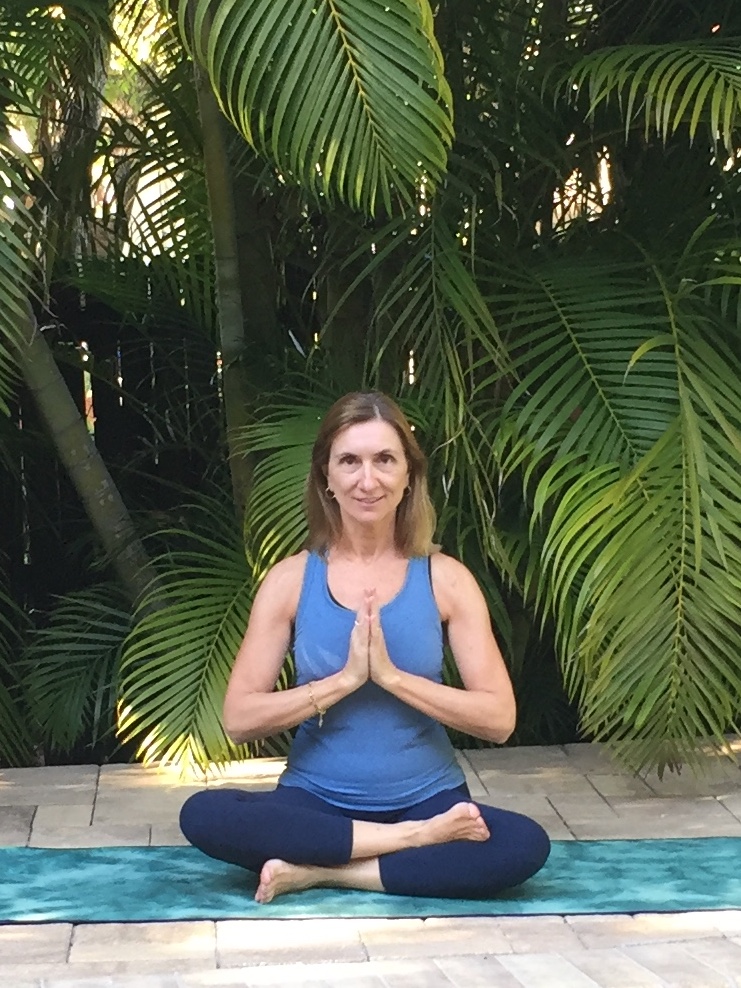 woman sitting on yoga mat in meditation pose with palm leaves behind her