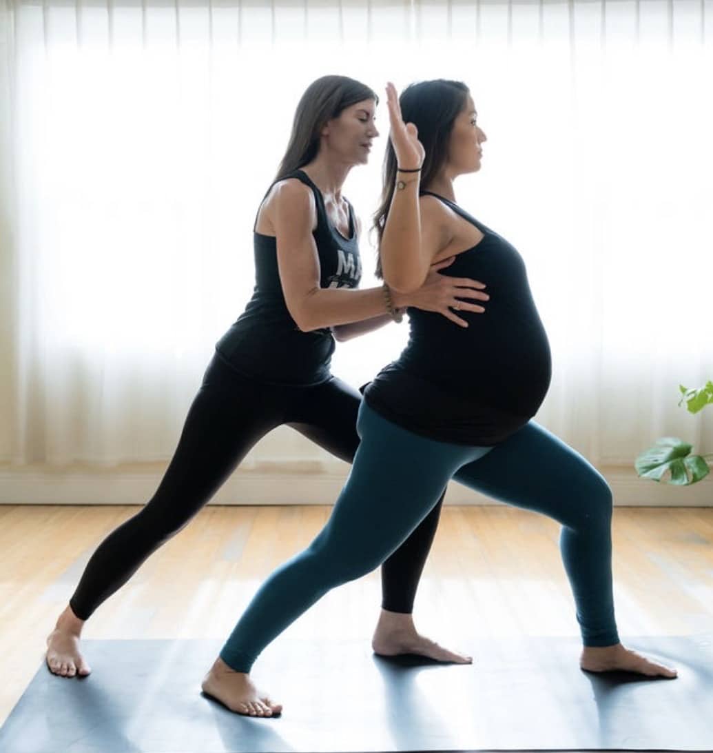 prenatal yoga instructor helping pregnant woman in yoga pose