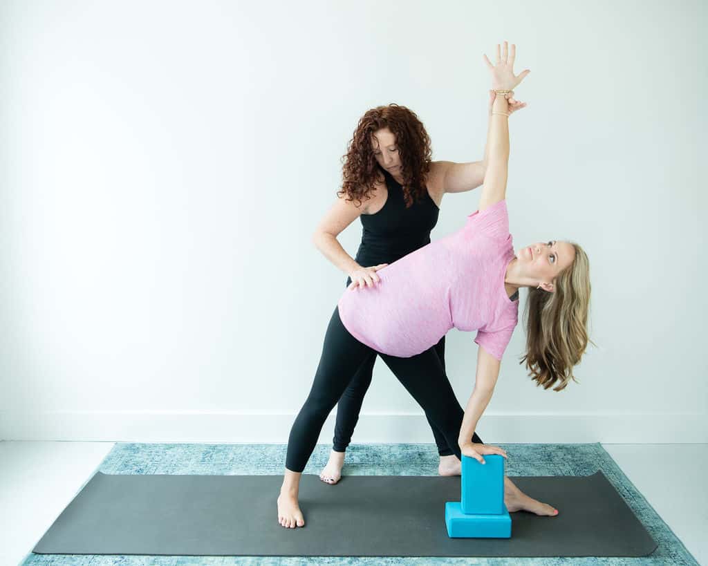 prenatal yoga instructor helping pregnant woman do a yoga pose